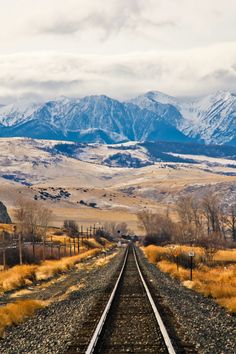 an empty train track in the middle of nowhere, with mountains in the back ground