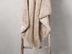 a chair with a blanket on top of it next to a wooden ladder in front of a gray wall