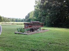 a sign in the middle of a grassy field with trees and bushes behind it,