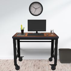 a computer desk with a clock on the wall above it and a trash can in front of it