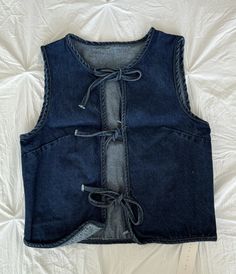 a blue jean vest with laces on the front and back, sitting on a bed