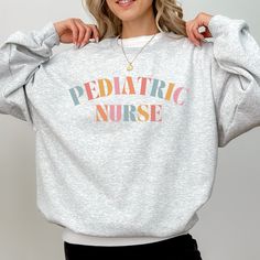 a woman wearing a grey sweatshirt with the words pediatric nurse printed on it in multi - colored letters