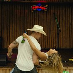 a man and woman dance together in front of a wooden wall with signs on it