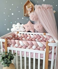 a baby crib with pink bedding and stars on the wall next to a potted plant