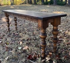 an old wooden table sitting in the middle of a field with leaves on the ground