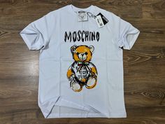 Features: * Oversized MOSCHINO short-sleeve t-shirt * Color: White with a playful, large teddy bear graphic and bold MOSCHINO logo on the front * Made from premium, high-quality fabric for a comfortable and relaxed fit * Crew neck design for a classic yet modern look * Unique and durable print that adds a fun, stylish statement to any wardrobe Oversized Teddy Bear, Teddy Bear Graphic, Large Teddy Bear, Moschino Logo, Shirt Oversize, T Shirt Oversize, Bear Graphic, Un Logo, T Shirt Oversized