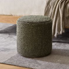 a round ottoman sitting on top of a rug next to a bed