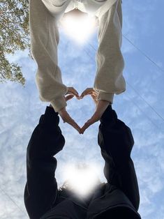 two people making a heart with their hands in front of the sun and blue sky