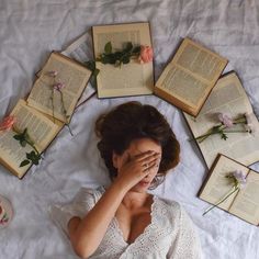 a woman laying on top of a bed covered in books and flowers next to an open book