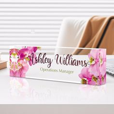 a pink flowered business name plate sitting on top of a desk next to a laptop