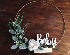 a wooden sign that says baby with flowers and greenery