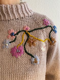 a woman wearing a sweater with flowers on the front and back of it, made out of yarn