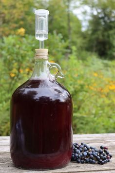 a glass jug filled with liquid sitting on top of a wooden table next to berries