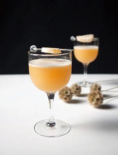 two glasses filled with orange juice and garnished with lemon peels on a white table