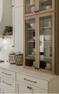 a cabinet with glass doors in the middle of a white kitchen counter top and cabinets below it