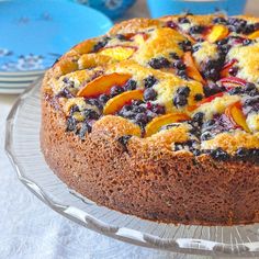 a cake with blueberries, peaches and other toppings on a glass platter