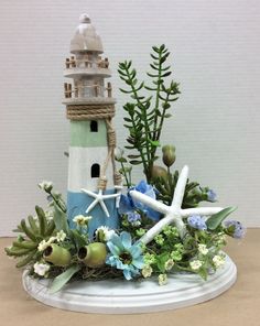 an arrangement of flowers and seashells is displayed on a white plate with a lighthouse in the background