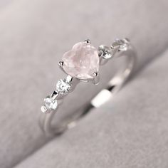 an engagement ring with a heart shaped pink stone and three diamonds on the band, set in white gold