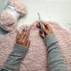 a woman is crocheting on a pink blanket with her hands and nails in the middle