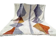 a multicolored blanket with fringes on it and an orange, blue, yellow, purple, and white design