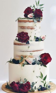 a three tiered wedding cake with red roses on top and greenery around the edges