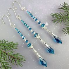 three pairs of blue crystal earrings hanging from silver earwires next to evergreen branches