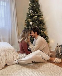 a man and woman sitting on the floor in front of a christmas tree