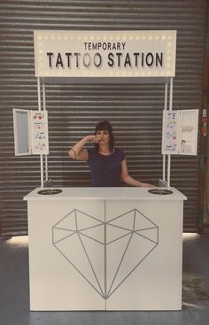 a woman standing behind a tattoo station with her hand on her chin and looking at the camera