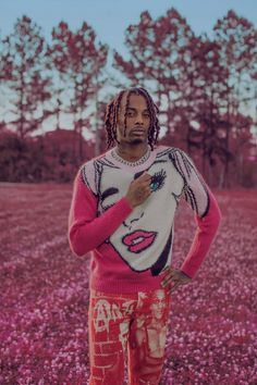 a man with dreadlocks standing in the middle of a pink flower covered field