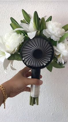 a hand holding a fan with white flowers in front of a wall and ceiling light