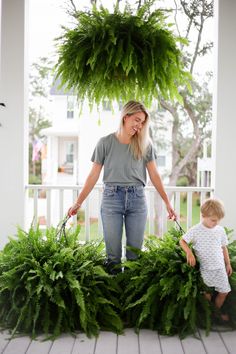 a woman and her child are standing on the porch with plants hanging from the ceiling