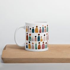 a white coffee mug with multicolored people on it sitting on a wooden table