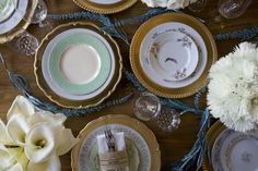 the table is set with white and gold plates, silverware, and flower centerpieces