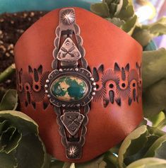 a brown leather cuff with an image of the earth on it, surrounded by succulents