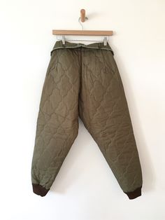 Quilted military liner pants in olive green. Fabric: nylon/ poly fill Fit: S|M Measurements:Waist adjustable 24”-32" Hips 43" Rise 14.5" Inseam 27.5" Length 40.5" Condition: Excellent Military Style Olive Parachute Pants With Pockets, Utility Parachute Pants For Winter, Green Military Style Parachute Pants, Military Nylon Outdoor Pants, Green Combat Style Long Pants, Green Combat Long Pants, Winter Utility Nylon Parachute Pants, Military Style Parachute Trousers For Outdoor, Green Military-style Long Pants