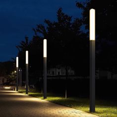 several lights are lit up on the side of a walkway at night time, with grass and trees in the background