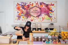 a woman standing behind a counter in front of a sign that says the raw chemist