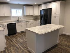 an empty kitchen with white cabinets and granite counter tops, black refrigerator and dishwasher