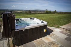 a hot tub sitting on top of a stone patio next to a lush green field