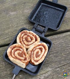 two cinnamon rolls in a black pan on a picnic table next to an electric grill