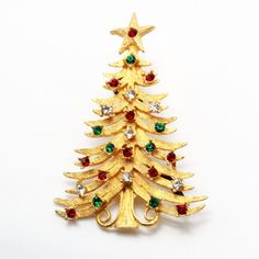 "DESCRIPTION: This exquisite vintage designer brooch by Mylu, dating back to the 1960s, is a captivating representation of holiday elegance. The Christmas tree motif, crafted from a lustrous gold-tone metal base with textured finishing, is adorned with a harmonious blend of red, green, and crystal rhinestones that glisten with festive allure. In impeccable mint condition and marked with the signature \"MYLU,\" this brooch measures a graceful 2.5\" in length, making it a timeless and cherished ac Designer Brooch, Gold Tree, Christmas Pins, Vintage Designer, Gold Texture, Metal Base, Gold Tone Metal, Christmas Decor Diy, Crystal Rhinestone