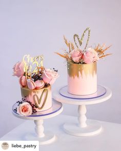 two cakes decorated with pink and gold frosting on top of white pedestals, one has the word love written on it