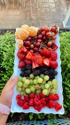 a person holding up a platter with fruit on it in front of some bushes