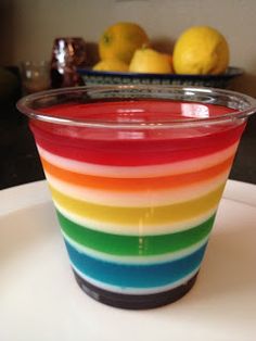 a rainbow colored cup sitting on top of a white plate next to some lemons