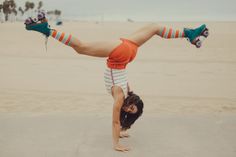 a woman doing a handstand on the beach with her feet in the air