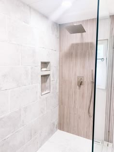 a walk in shower sitting next to a white tiled wall and floor with a glass door