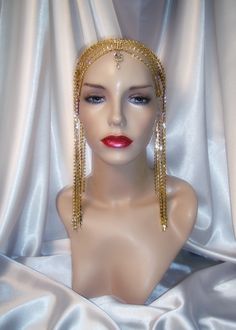 "This luxurious headpiece features layers of brilliant gold rhinestones that drape down the sides and back, encircling the head for a dramatic effect. A brilliant rhinestone pendant accents the center of the headpiece for added luster (pendant may vary in size and shape). The piece is held in place with a rhinestone trimmed headband and its weightiness allows it to sit comfortably atop the head with the assistance of hair/bobby pins. This piece is both elegant and stylish, suitable for formal or Gold Goddess Headpiece For Party, Gold Goddess Headpieces For Wedding, Gold Rhinestone Headpieces For Party, Gold Goddess Wedding Headpieces, Gold Rhinestone Body Jewelry For Wedding, Adjustable Gold Hair Accessories For Festivals, Glamorous Gold Body Jewelry With Rhinestones, Glamorous Gold Wedding Headpiece, Adjustable Gold Body Jewelry With Rhinestones