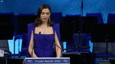 a woman in a blue dress standing at a podium with microphones and speakers behind her