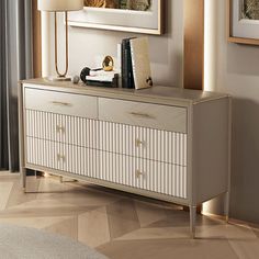 a white and gold dresser in a living room with pictures on the wall behind it