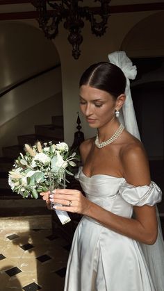 a woman in a wedding dress holding a bouquet of flowers and looking at the camera